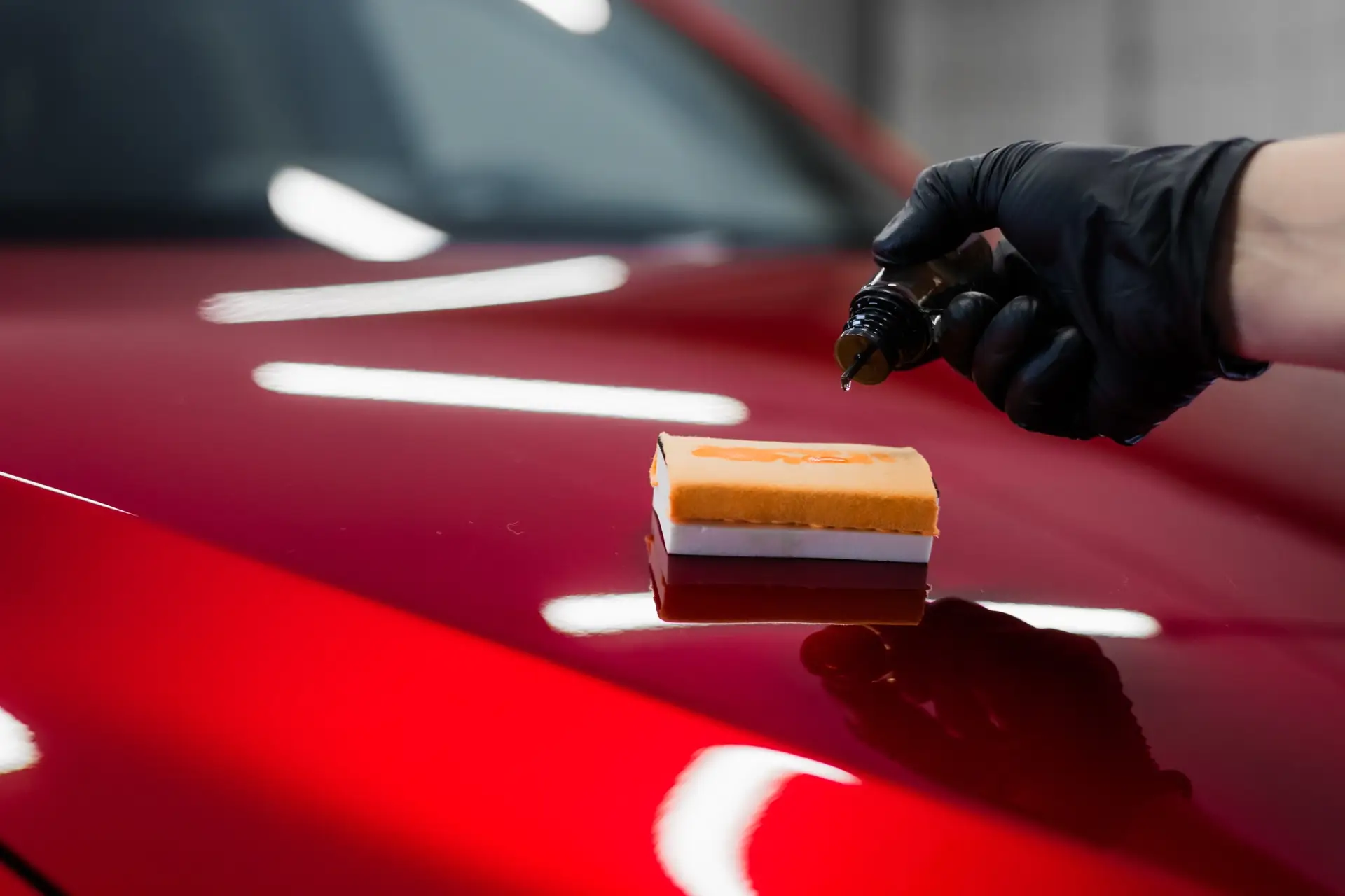 Car detailing - Man applies nano protective coating or wax on red car. Covering car bonnet with a