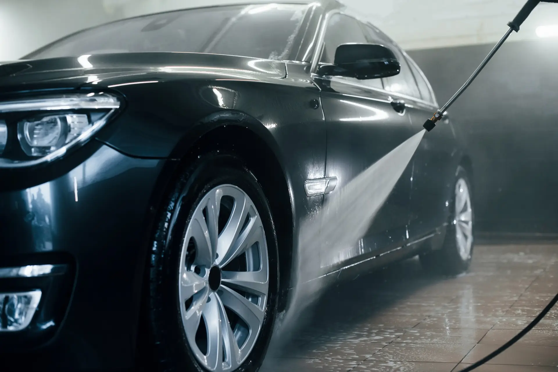 High pressured water. Modern black automobile get cleaned inside of car wash station